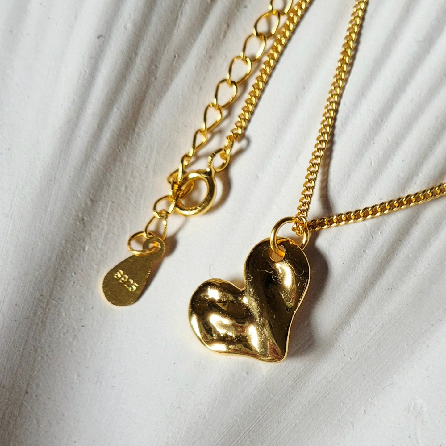 Sorella of May Gold heart-shaped pendant necklace on a textured white background
