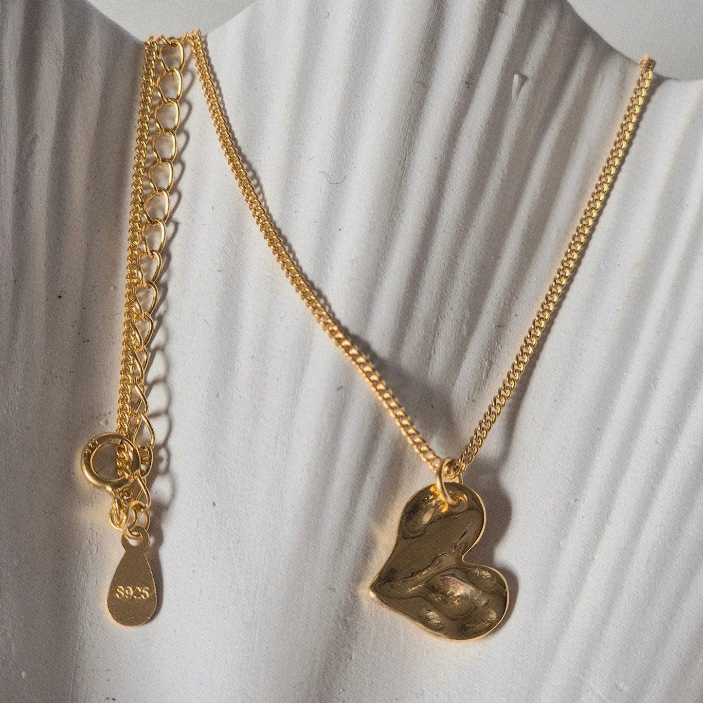 Sorella of May Gold chain necklace with a heart pendant resting on a prop