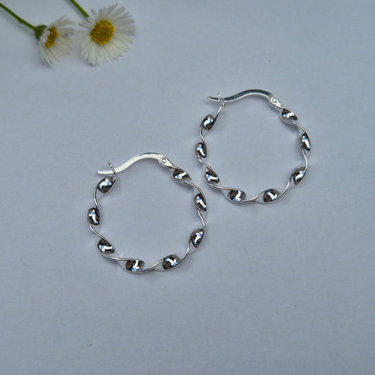 Silver Dakota hoop earrings on a light gray background with a small white flower.
