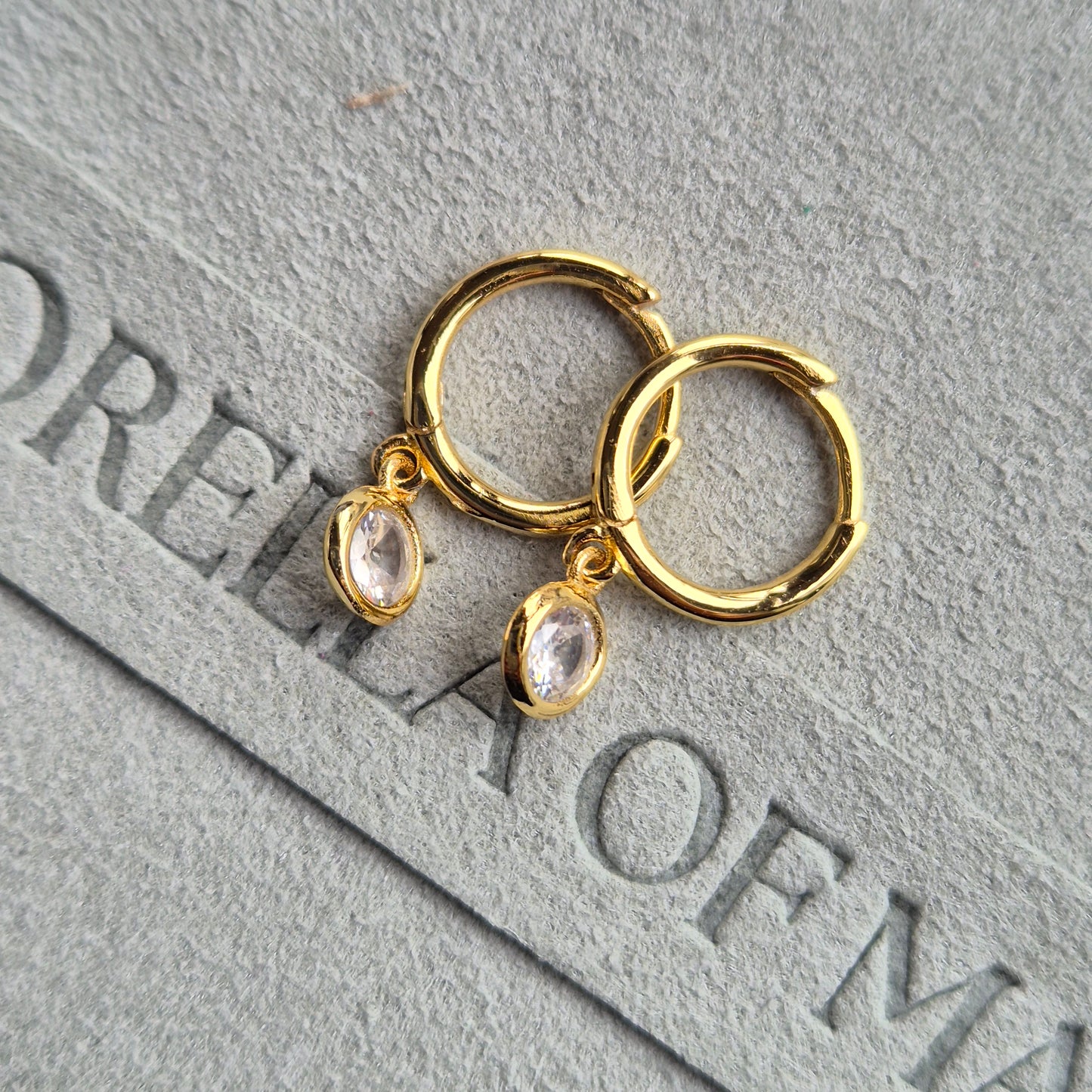 The Lumi huggie with a circular zirconia stone, laying flat on fabric