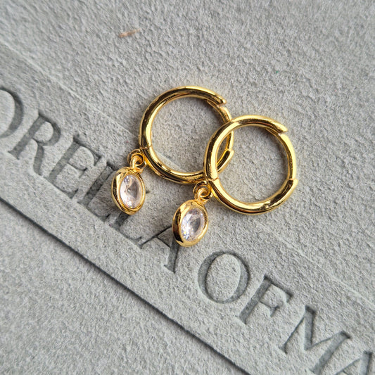 The Lumi huggie with a circular zirconia stone, laying flat on fabric