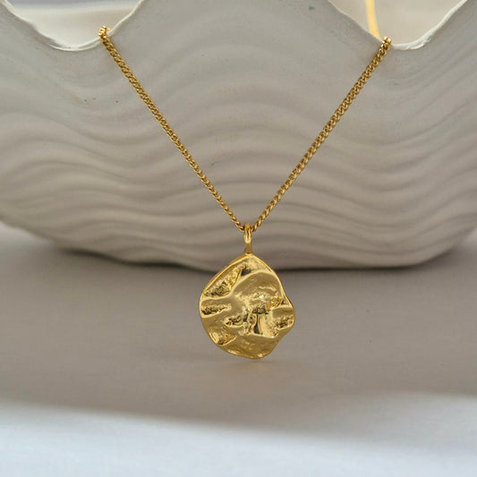 Gold necklace with the Maris pendant on a neutral background