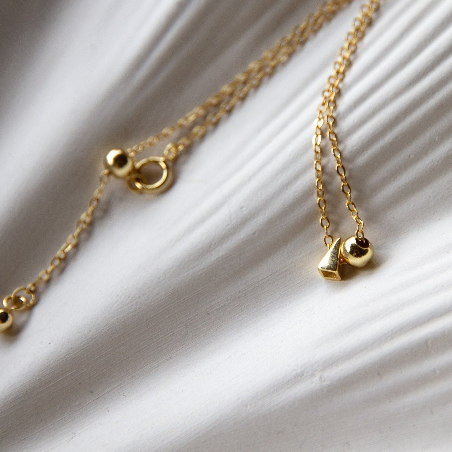 minimalist necklace with two tiny pendants, one a sphere, the other a pyramid, resting on a jewelry dish