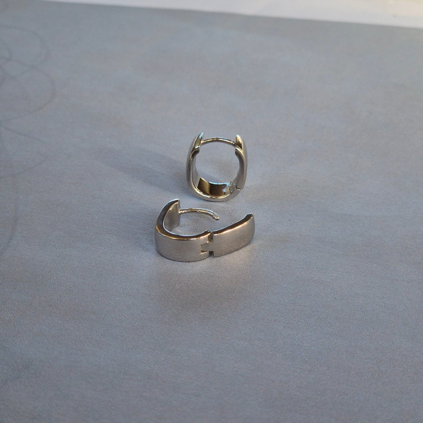 Sorellla of May sterling silver huggie earrings sitting on plain backgraoun