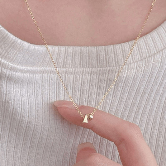 Gold necklace with a small pyramid and sphere pendant worn by a person on a light background