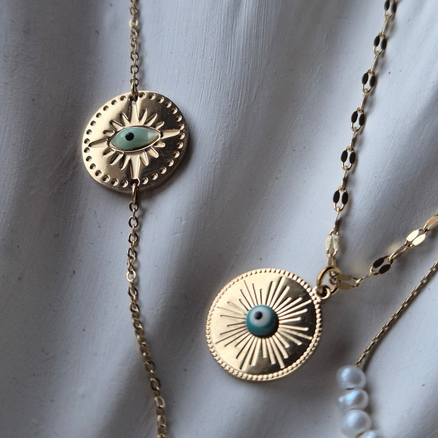 Sorella of May Gold bracelet and necklace both with evil eye pendant on cream colfabric background