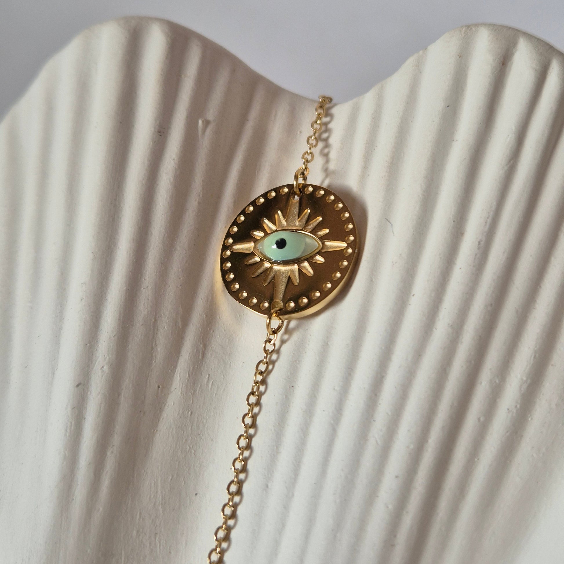 Sorella of May Gold bracelet with an Evil Eye pendant on a textured white surface