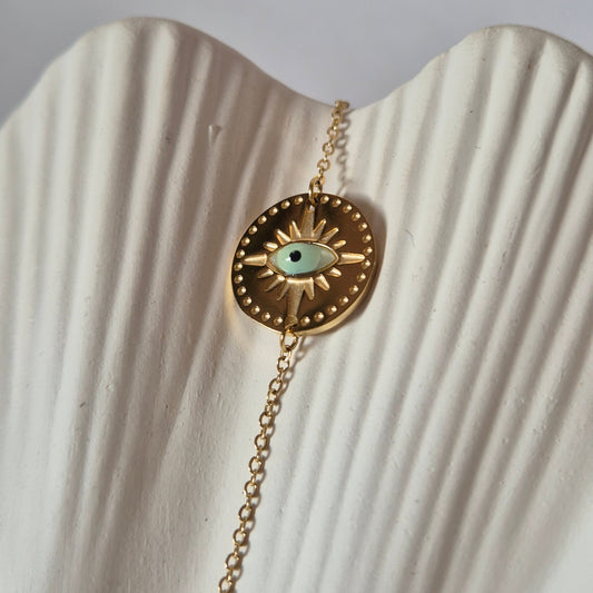 Sorella of May Gold bracelet with an Evil Eye pendant on a textured white surface