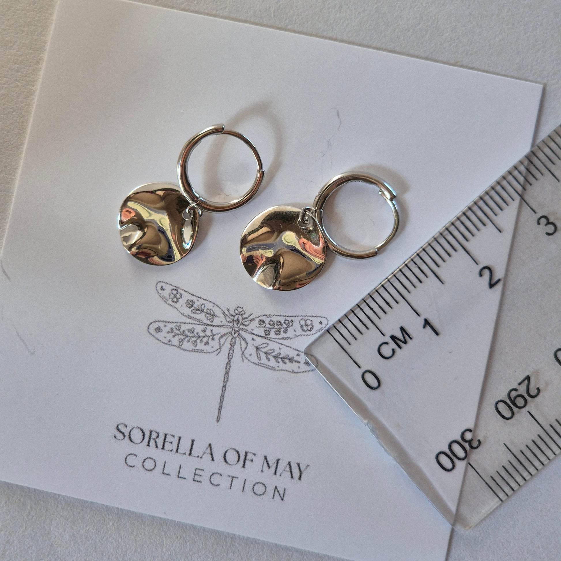 Two Sterling Silver Earrings resting on card with ruler next to earrings with measurement of 2cm long.  Earrings have small circular discs on huggie style earring 