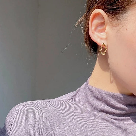 Close-up of a person wearing a gold hoop earring against a neutral background