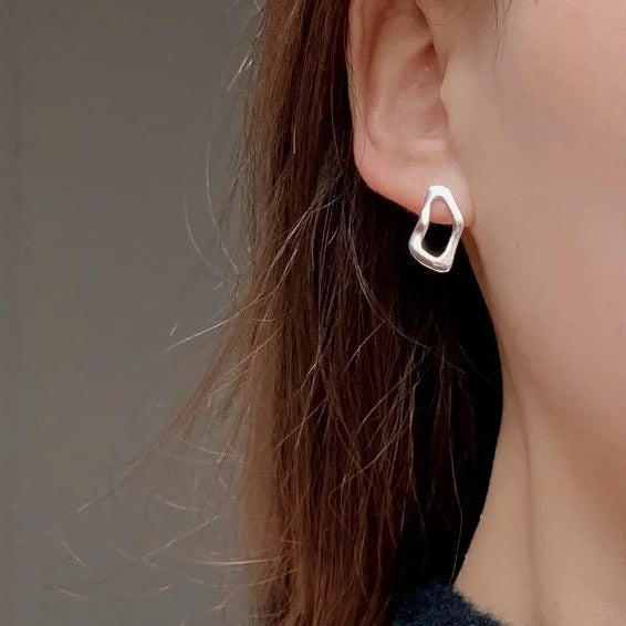 Silver hoop earring worn by a person with brown hair against a neutral background