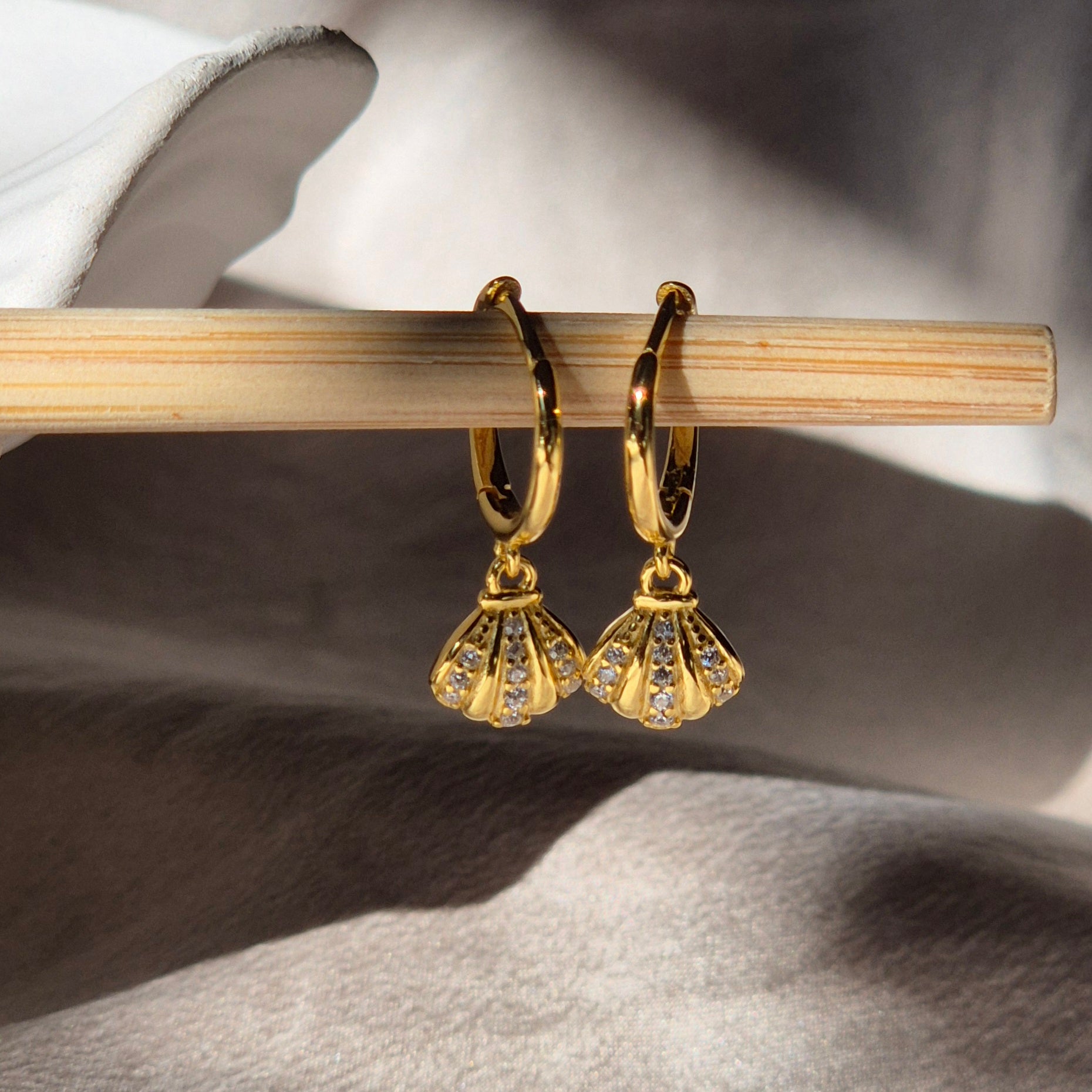 Gold earrings with fan-shaped design on a wooden stick against a neutral background