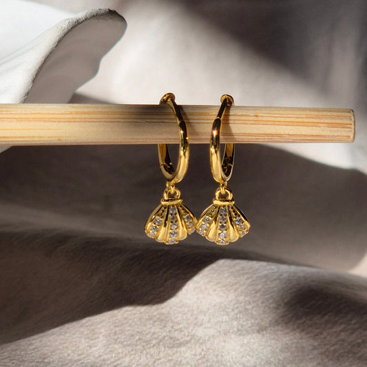 Gold earrings with fan-shaped design on a wooden stick against a neutral background