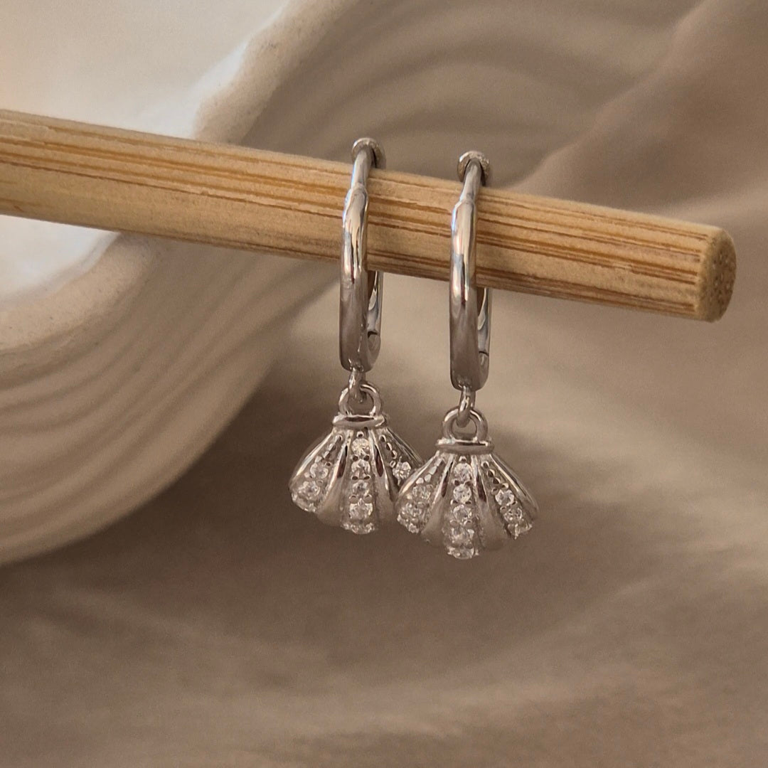 Silver earrings with fan-shaped designs hanging from a wooden stick.