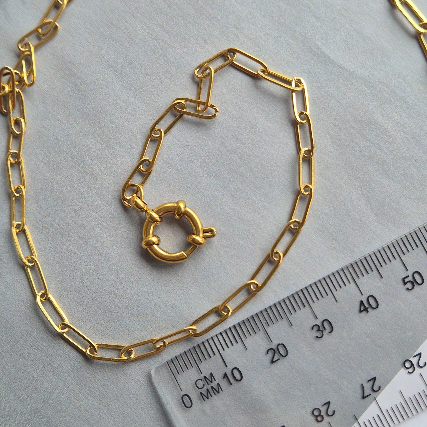 Sorella of May Noa paperclip gold necklace besides a ruler