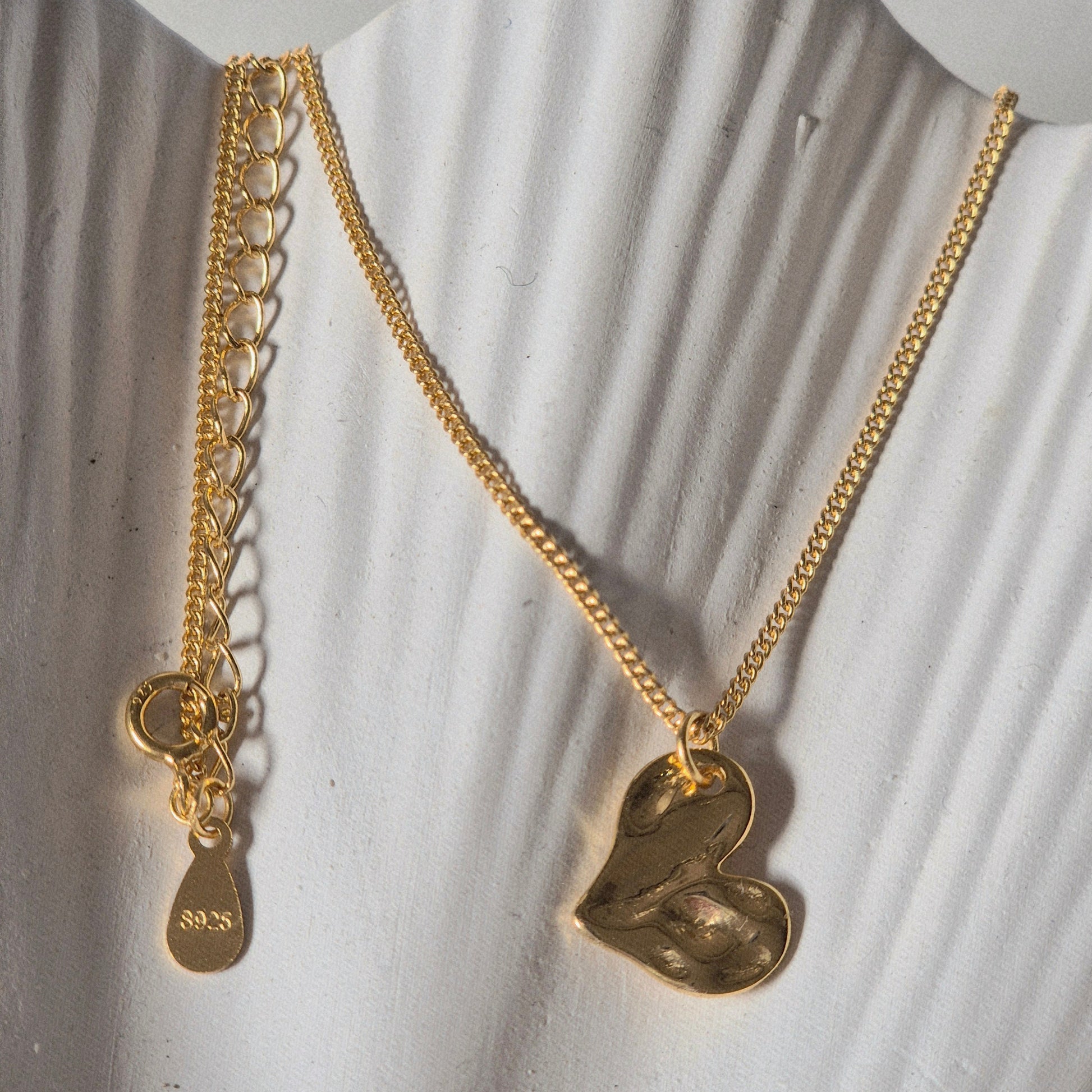 Sorella of May Gold chain necklace with a heart pendant resting on a prop