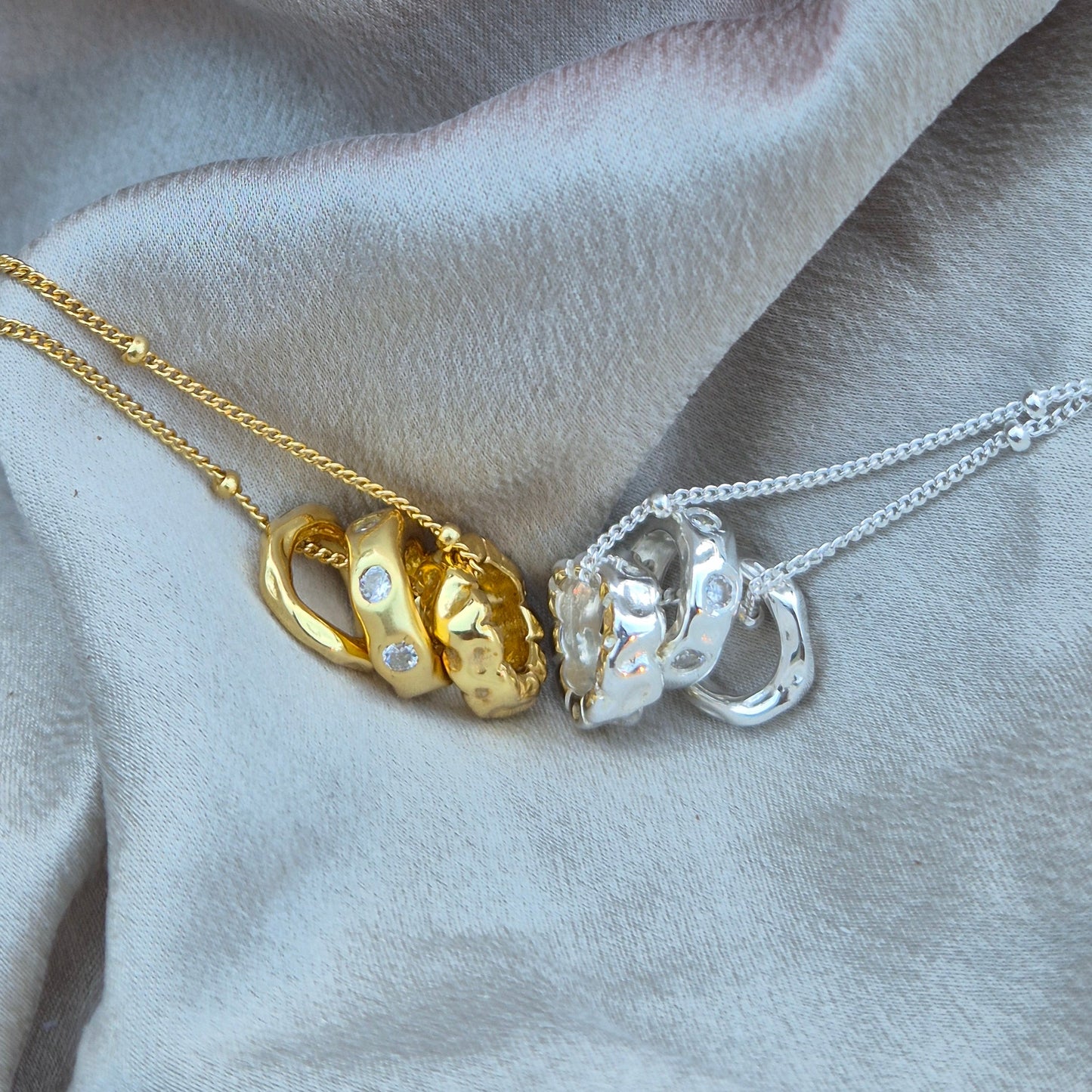 Sorella of May Eden 3 rings pendant necklaces in gold and silver laying beside each other on silk
