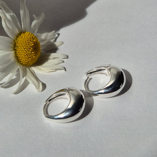 Silver hoop earrings next to a white daisy on a light gray background