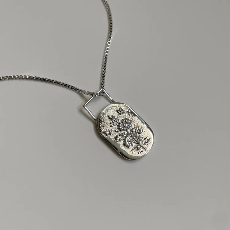 Silver necklace with a floral pendant on a gray background