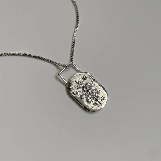 Silver necklace with a floral pendant on a gray background