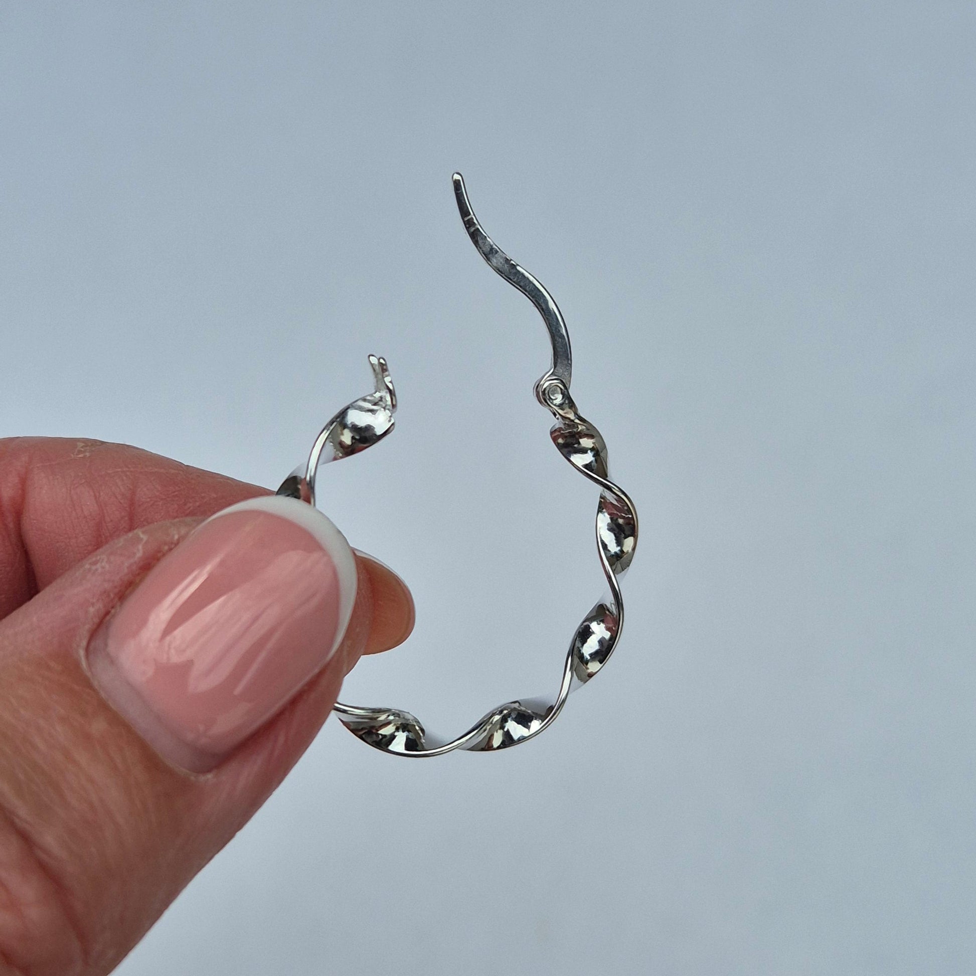 Silver Dakota earring being held by a hand against a light gray background