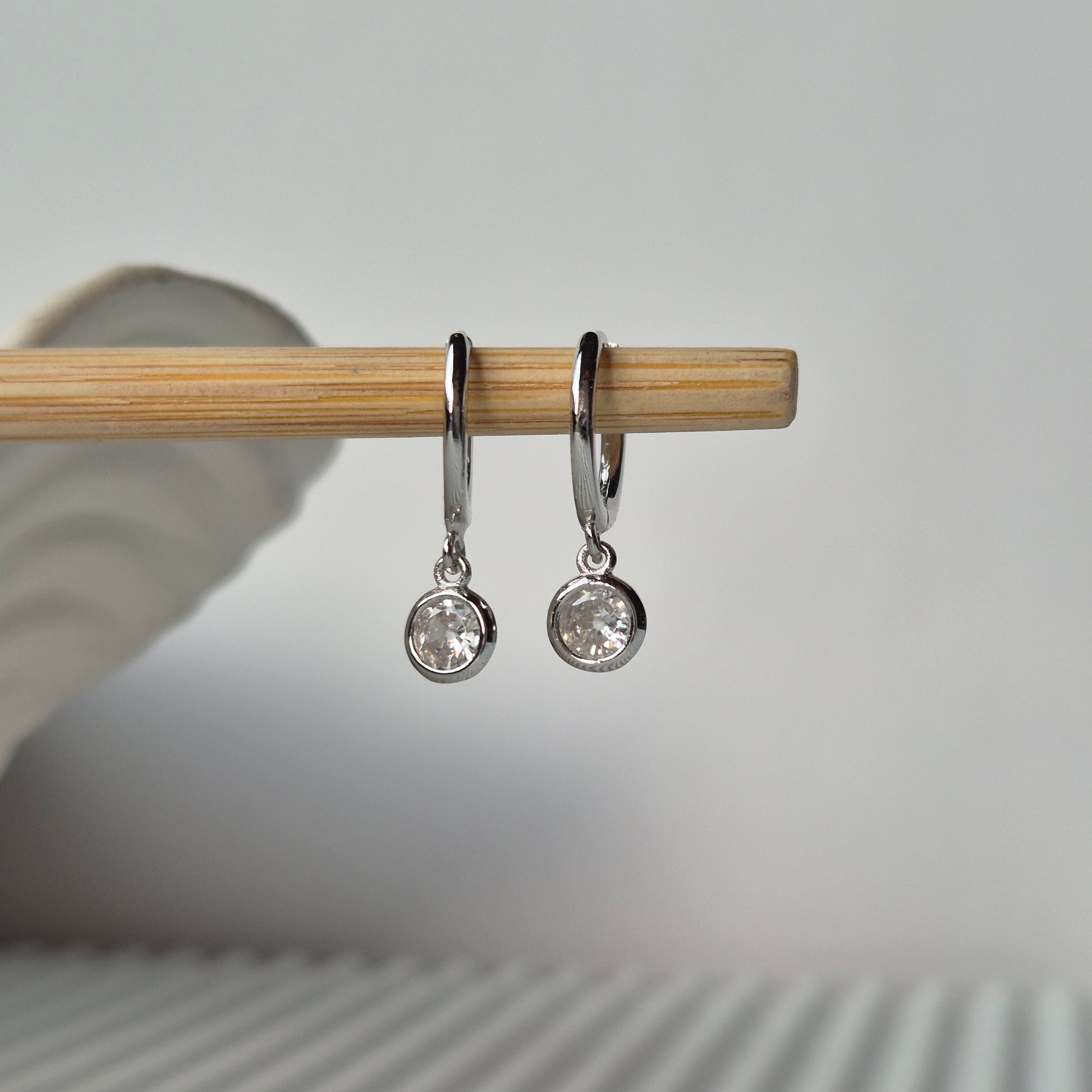 Two Lumi huggie earrings on a stick with grey tone background