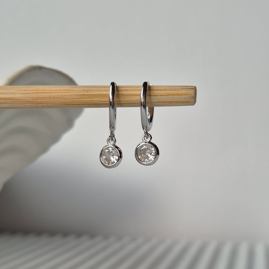 Two Lumi huggie earrings on a stick with grey tone background